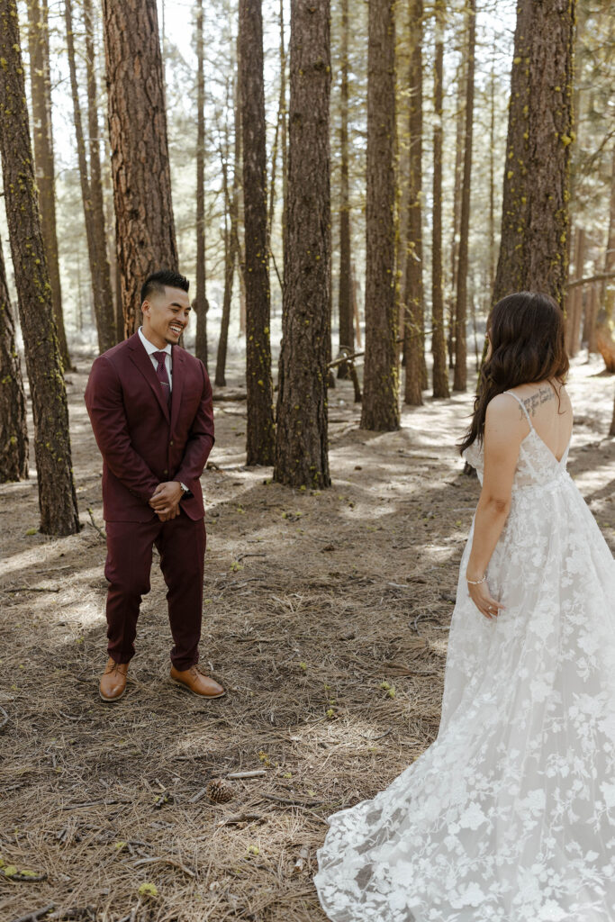 Wedding groom smiling while looking at bride with tall trees in background at Chalet View Lodge