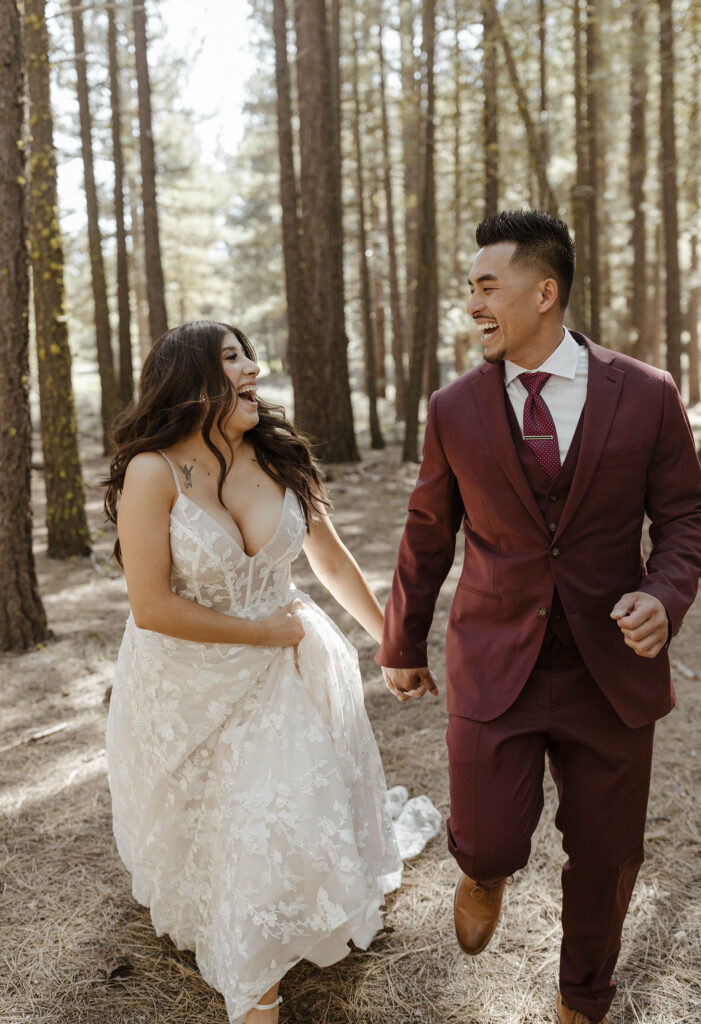 Wedding couple holding hands and walking through forest while smiling at each other outside of Chalet View Lodge