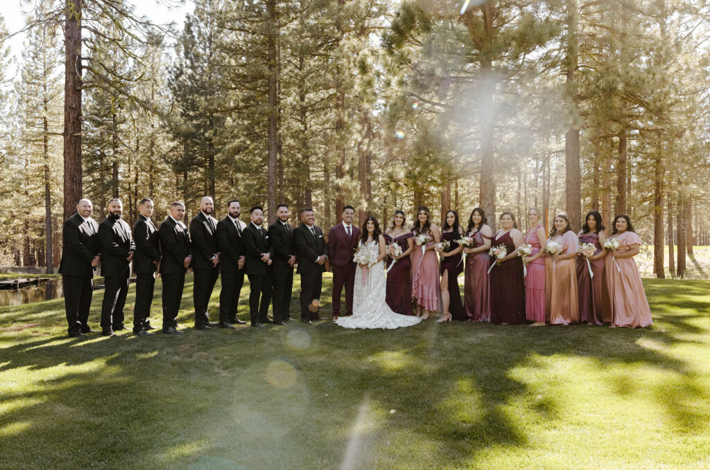 Wedding couple standing with bridesmaids and groomsmen smiling at camera with pine trees in background at Chalet View Lodge