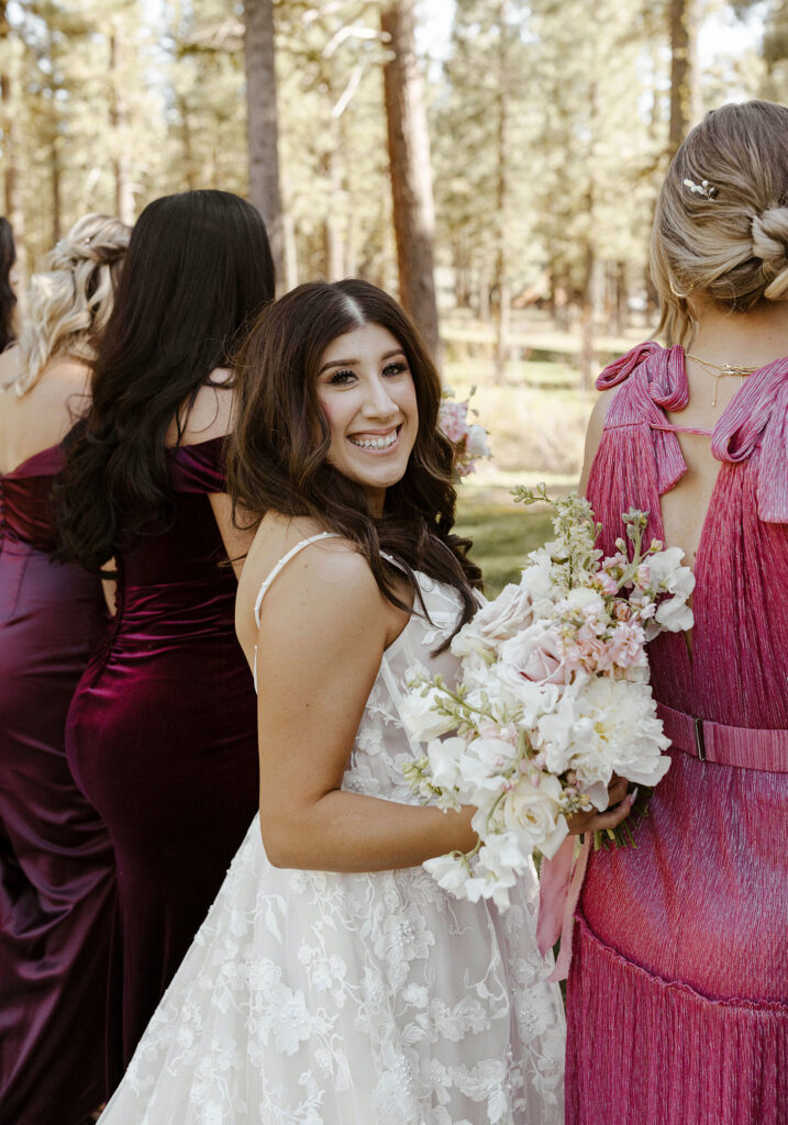 Wedding bride looking back over shoulder at camera while holding flower bouquet and standing with bridesmaids at Chalet View Lodge