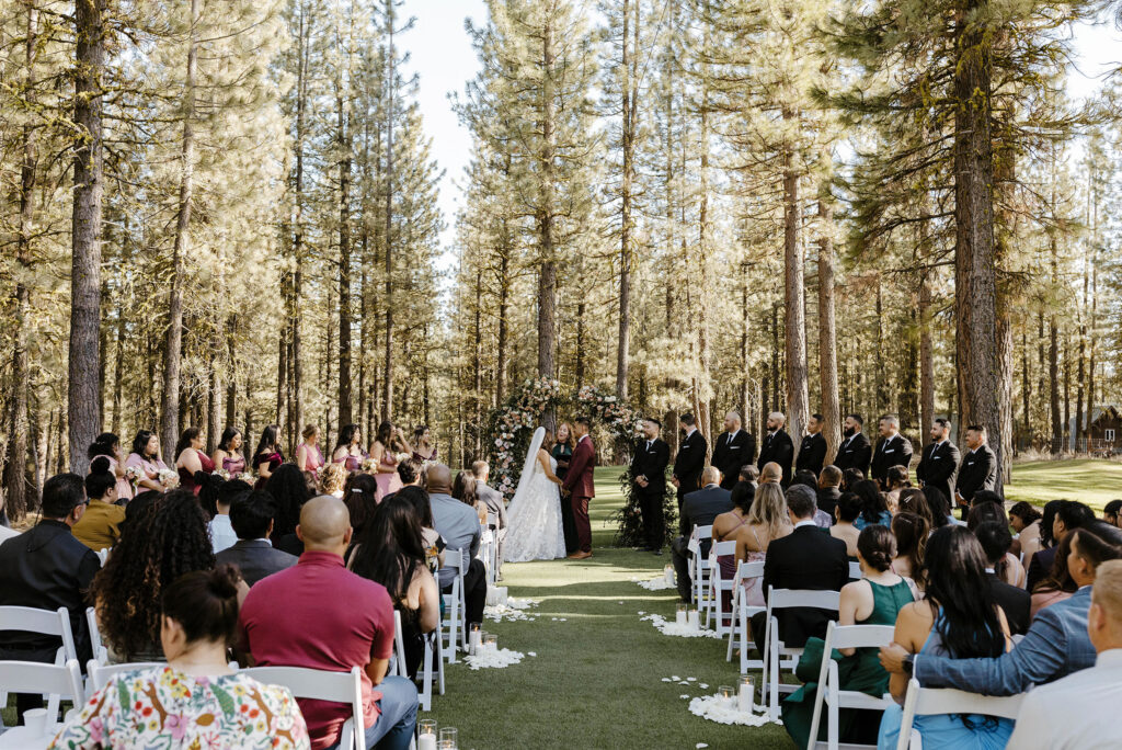 Overview of wedding ceremony with wedding couple and guests while surrounded by tall pine trees at Chalet View Lodge