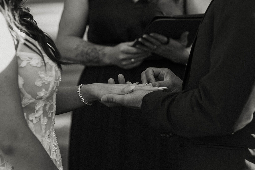 Groom sliding wedding ring onto bride's finger during ceremony at Chalet View Lodge