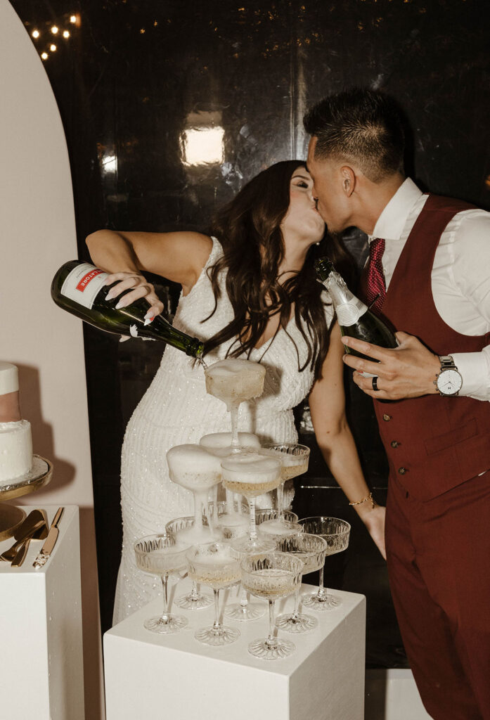 Bride pouring champagne into pyramid of glasses while kissing groom at Chalet View Lodge