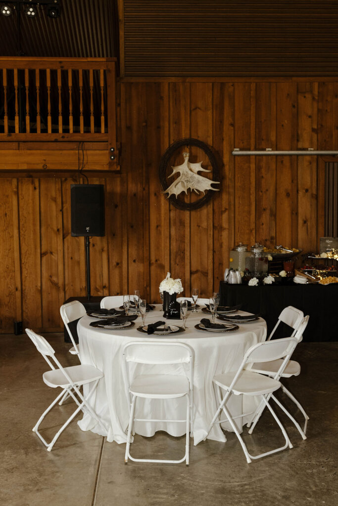 Wedding dinner table with white chairs and wooden wall in background at little bear creek ranch