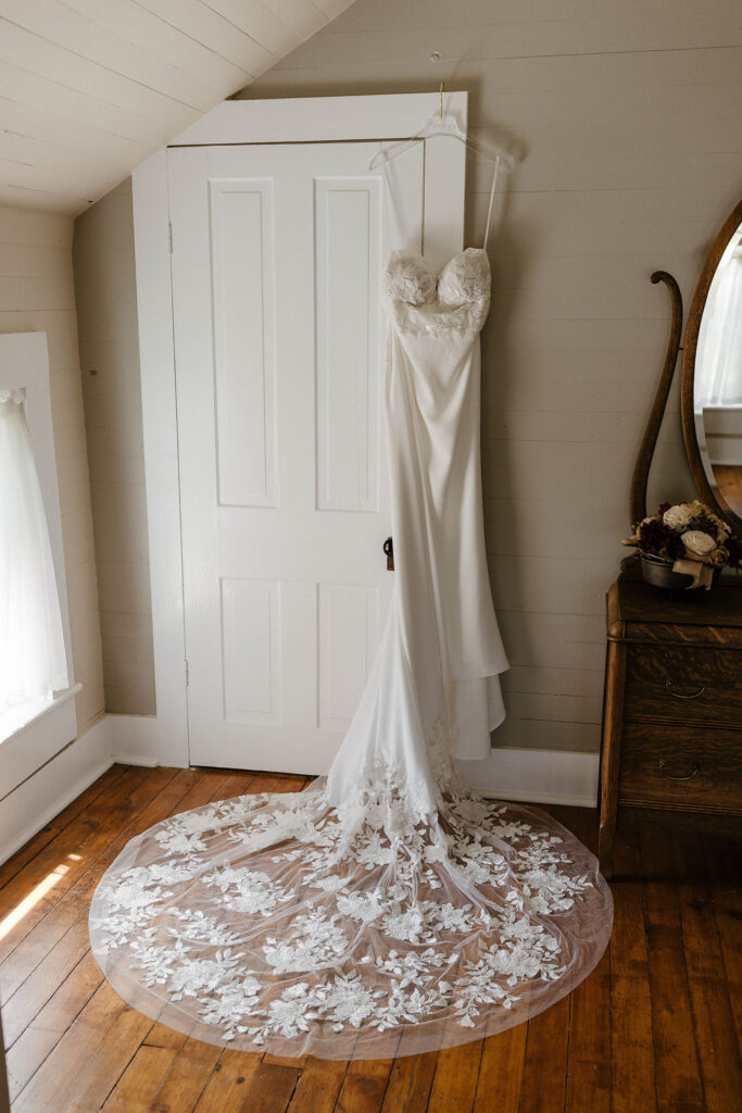 Wedding dress hanging on white door with lace trail spread out underneath at little bear creek ranch