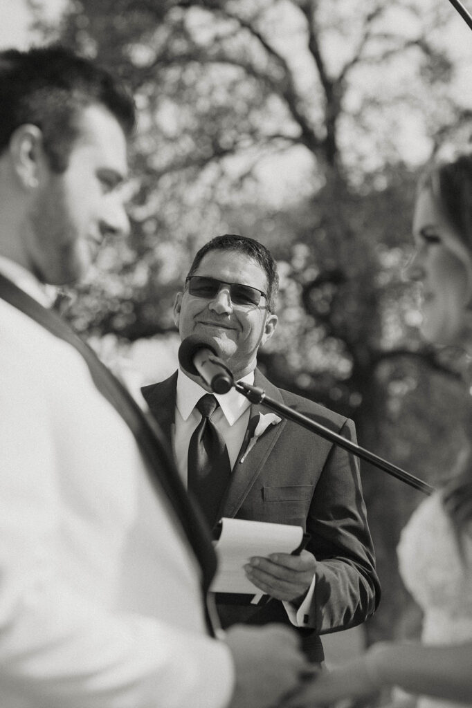 Brides dad as wedding officiant smiling at wedding couple during ceremony at little bear creek ranch