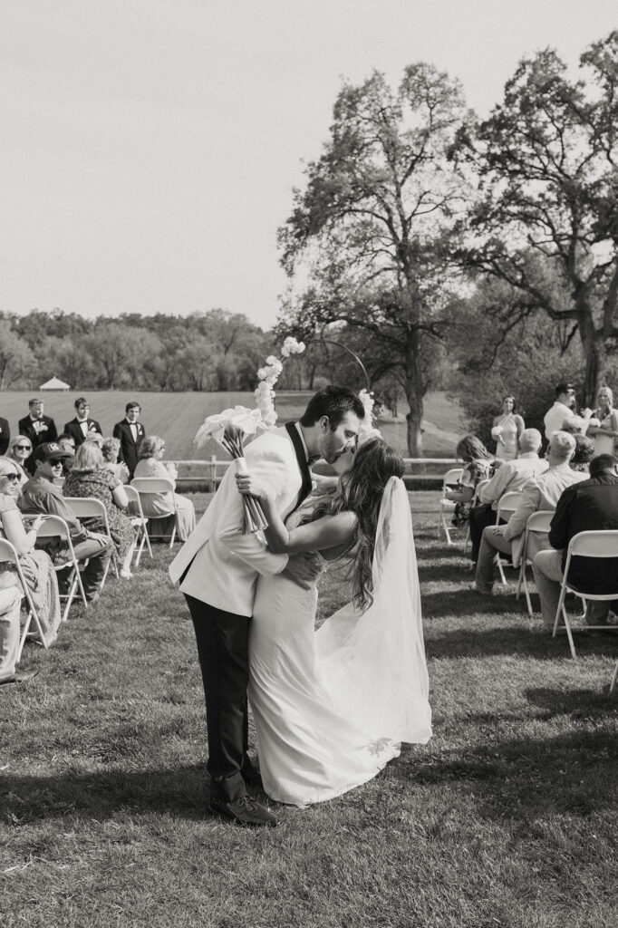 Wedding couple kissing in wedding aisle after ceremony at little bear creek ranch while bride holds flower bouquet