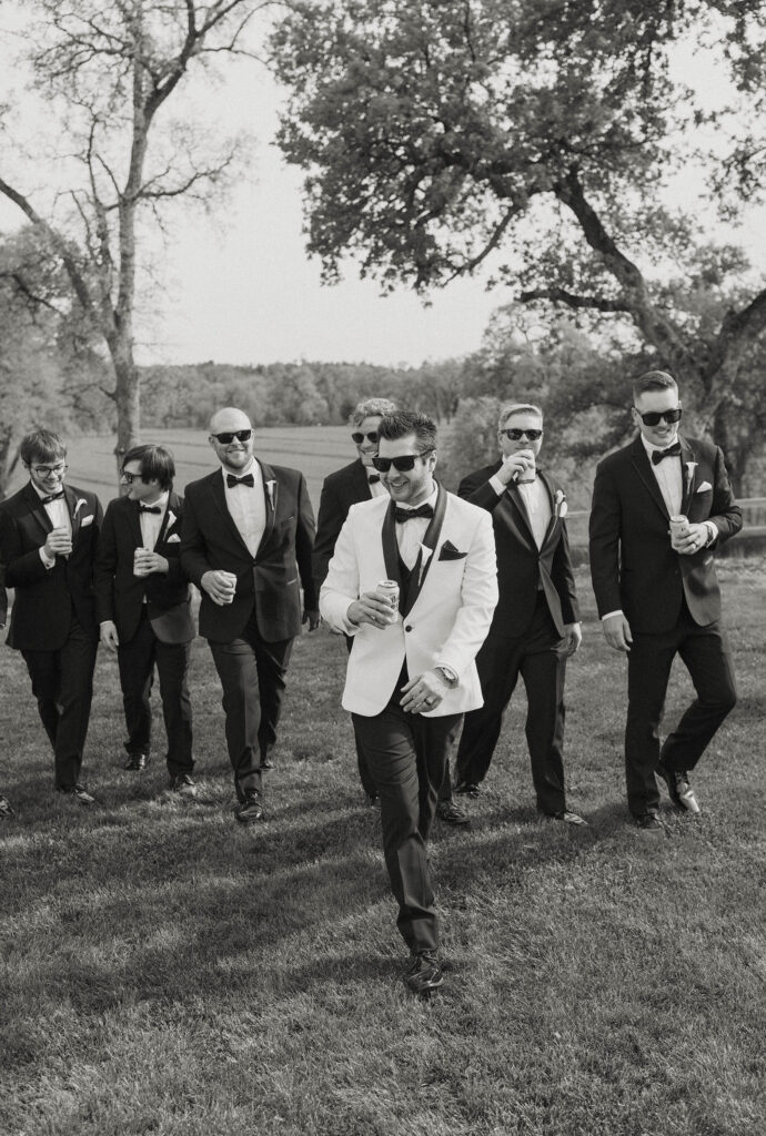 Wedding groom walking with groomsmen as all hold beers and walk toward camera at little bear creek ranch