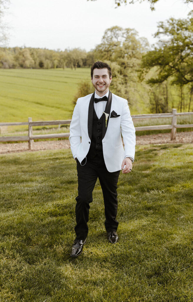 Wedding groom with hand in pocket walking towards and smiling at camera at little bear creek ranch
