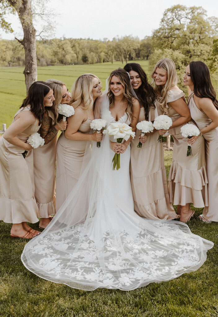 Wedding bride and bridesmaids holding flower bouquets and smiling outside at little bear creek ranch