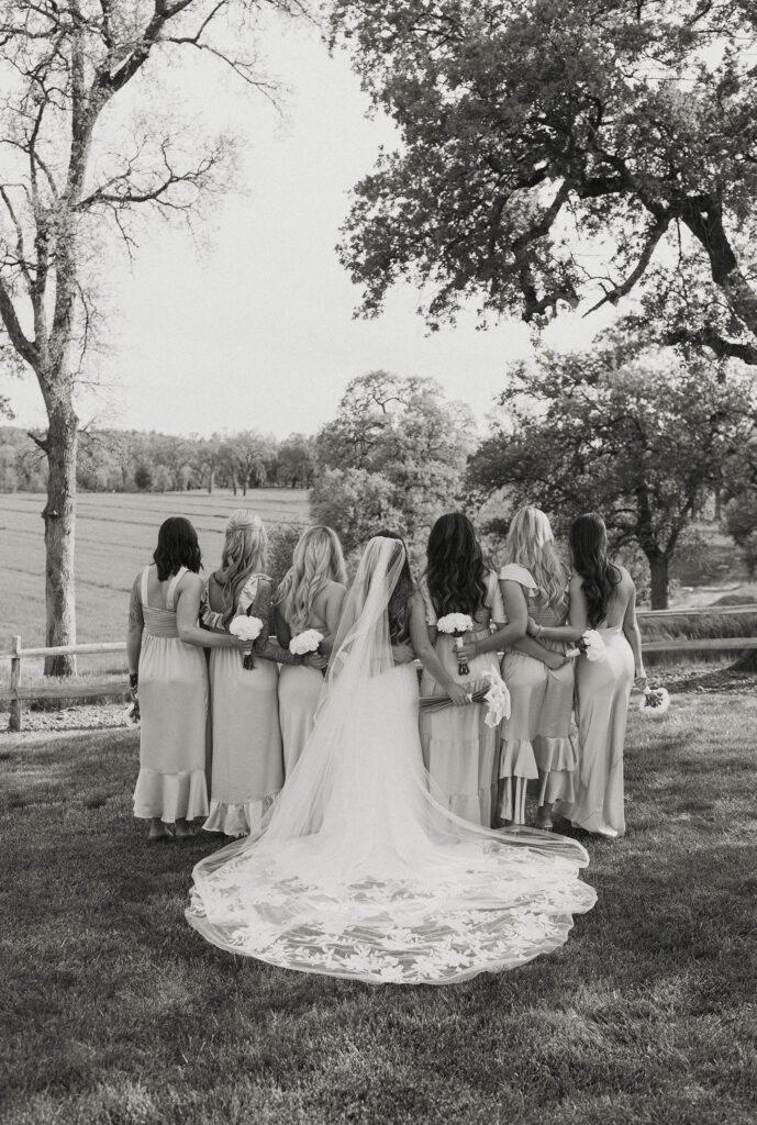 Bride and bridesmaids with arms around each other holding flower bouquets while looking away from camera at little bear creek ranch