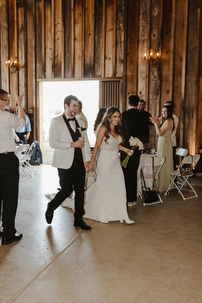 Wedding couple walking in to wedding reception while holding hands and smiling at guests at little bear creek ranch