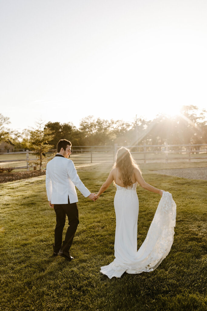 Wedding couple holding hands while walking away from the camera with trees and setting sun in background at little bear creek ranch