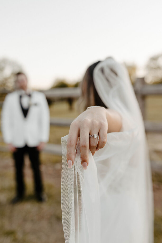 Close up of bride's hand with wedding ring as she holds veil out and looks at groom at little bear creek ranch
