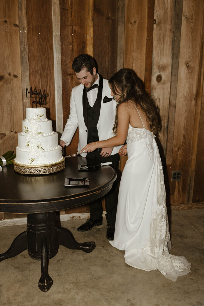 Wedding couple cutting wedding cake on wooden table together at little bear creek ranch