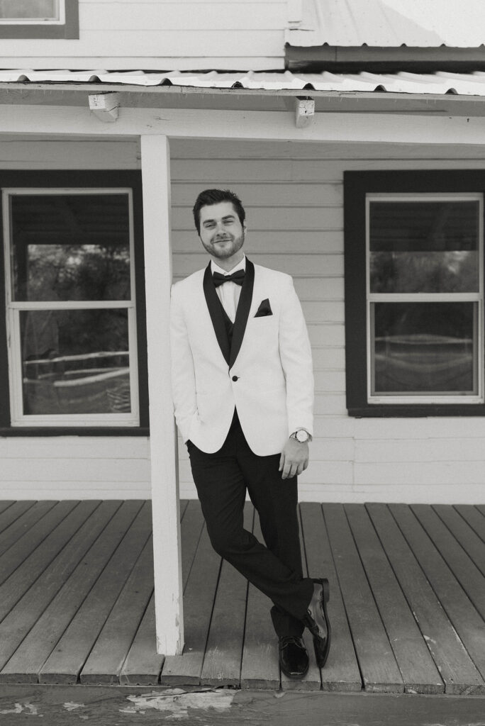 Wedding groom smiling at camera while leaning against pole on wooden porch at little bear creek ranch