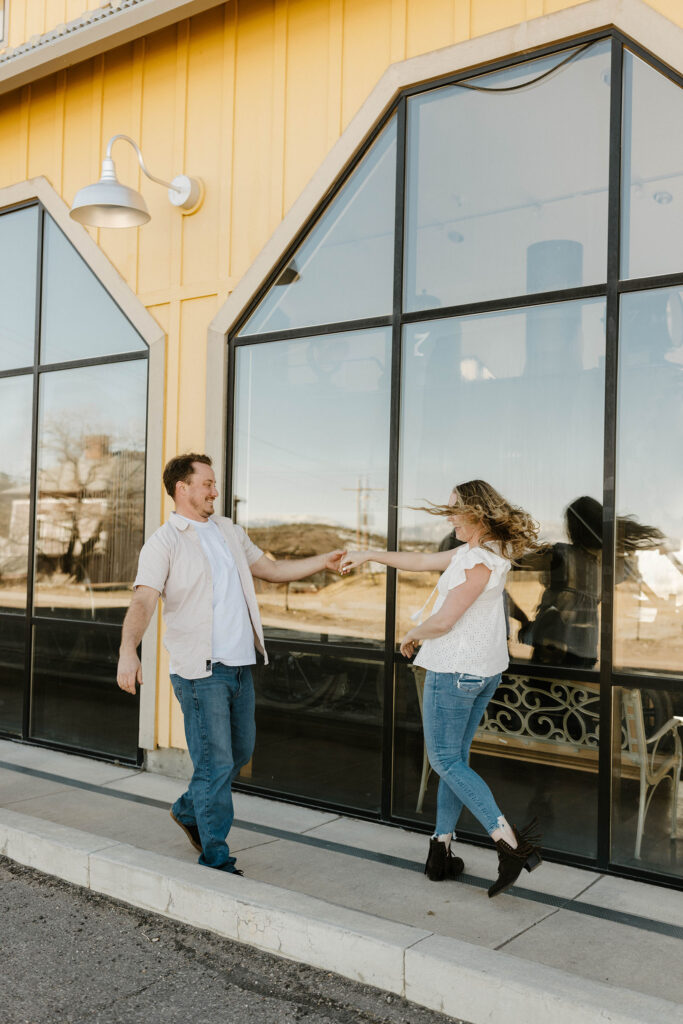 Engagement couple holding hands while dancing in front of large window in virginia city 