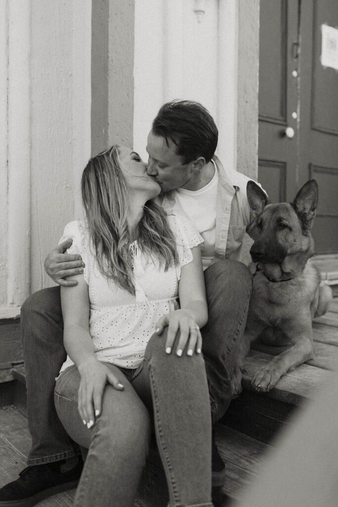 Engagement couple kissing while sitting on stairs with dog next to them in virginia city