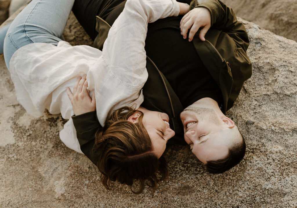 Engagement couple lying on rock while smiling and looking at each other at Logan Shoals