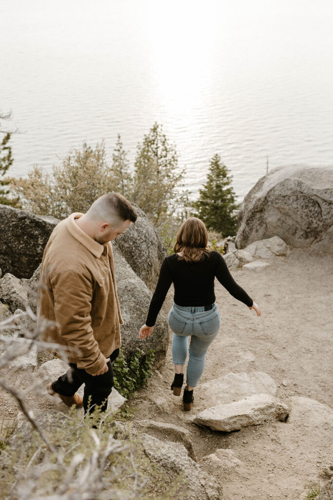 Engagement couple walking down rocks and away from camera together at Logan Shoals with Lake Tahoe in background
