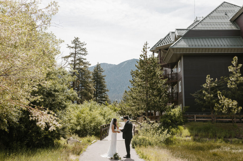 Elopement couple reading vows to each other while standing on walkway surrounded by trees with bridge in background in Lake Tahoe