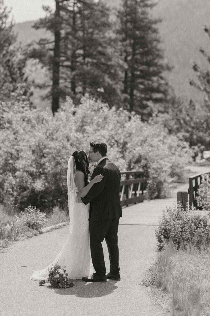 Elopement couple kissing while on walkway in Lake Tahoe surrounded by greenery with bridge in background