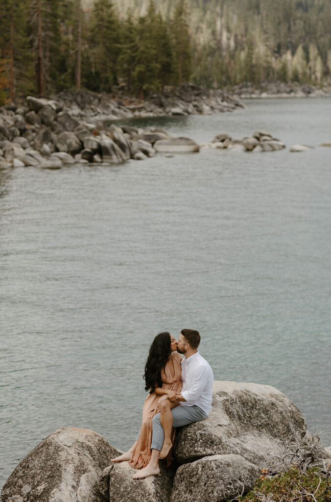Married couple sitting on large rock together overlooking Lake Tahoe with water in background