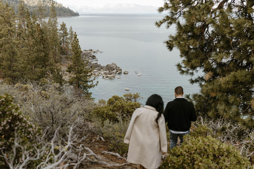 Married couple walking downhill on dirt path towards shore of Lake Tahoe