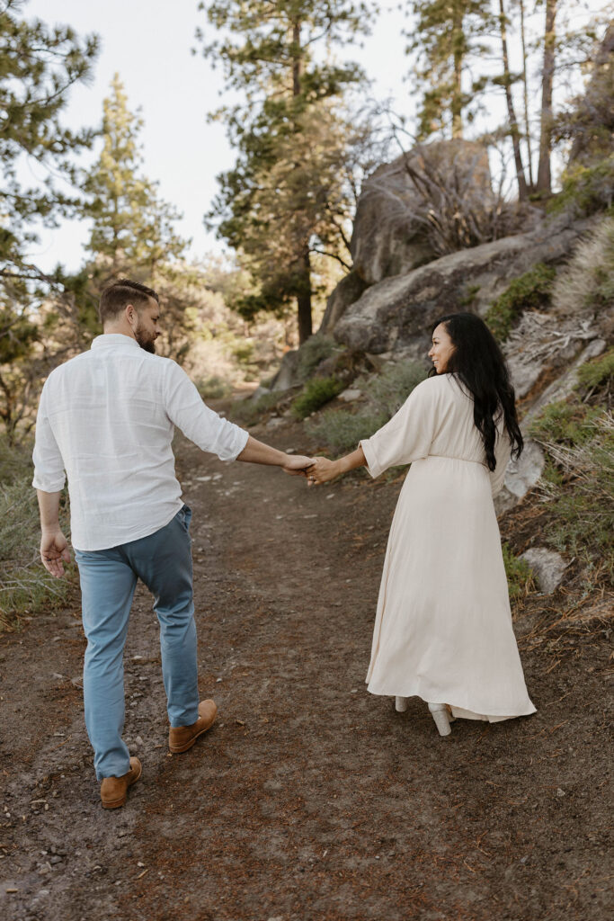 Married couple holding hands and looking at each other while smiling and walking up dirt trail together in Lake Tahoe