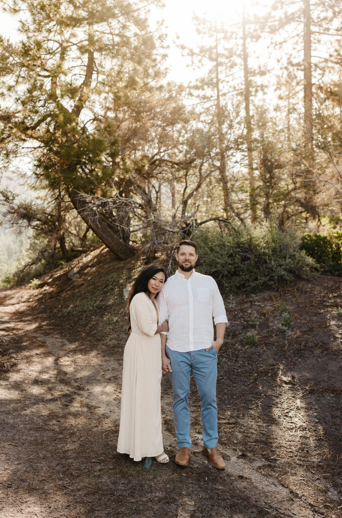 Married couple standing together and looking at camera while smiling with sun shining through trees in background at Lake Tahoe