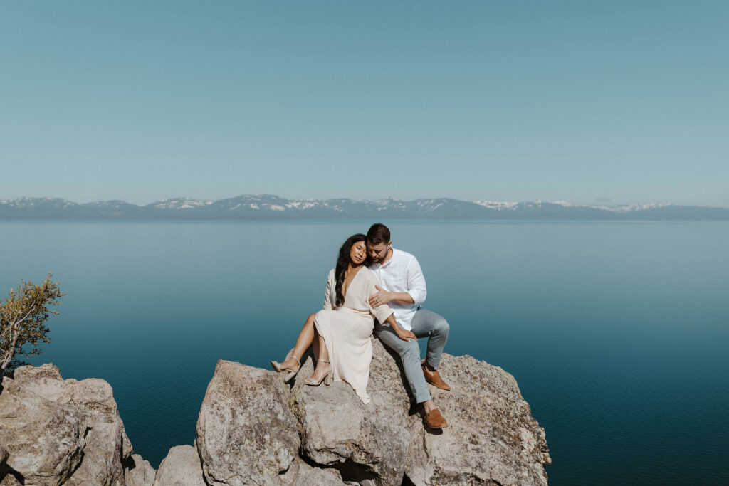 Married couple sitting on large rock together high above Lake Tahoe with lake and mountains in background