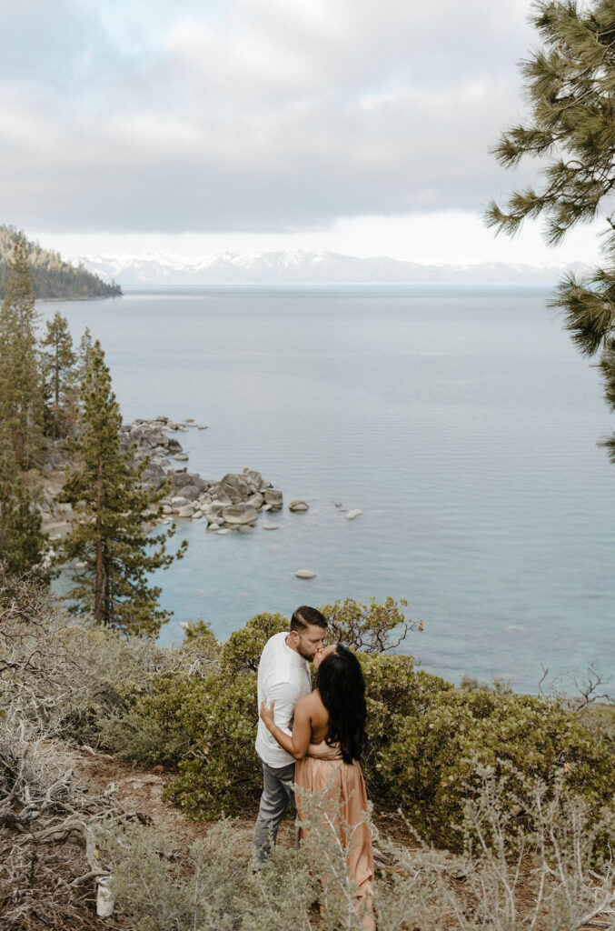Married couple kissing while holding each other on dirt trail overlooking Lake Tahoe