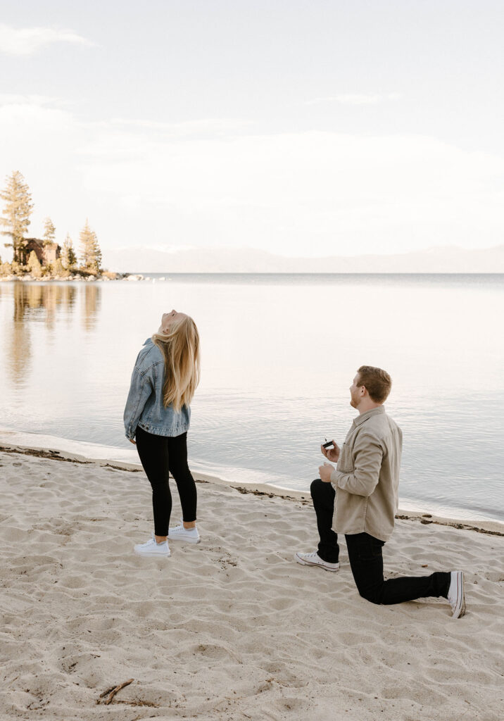 Man on one knee holding engagement ring while fiancé has back turned at Meeks Bay