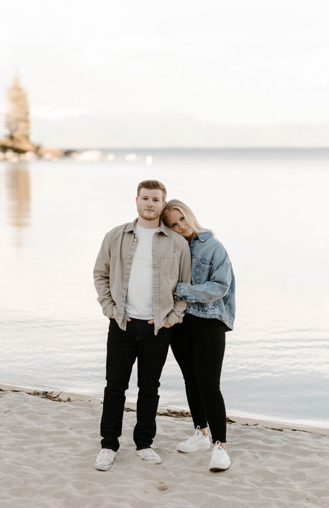 Engagement couple standing together while looking at camera at Meeks Bay with Lake Tahoe in background