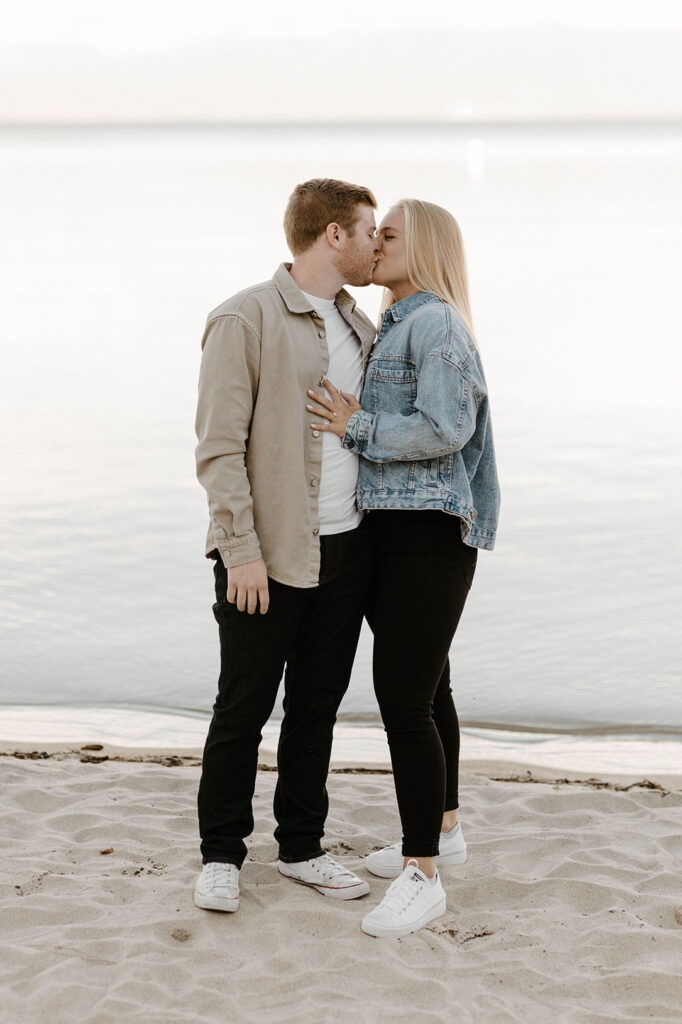 Engagement couple kissing while on sandy beach at Meeks Bay with Lake Tahoe in background
