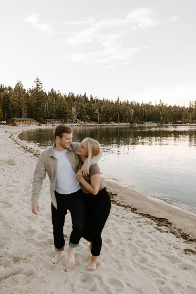 Engagement couple laughing and smiling at each other while walking down sandy beach together at Meeks Bay