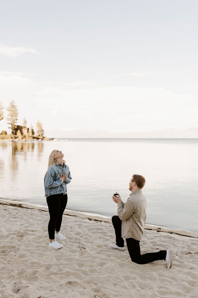 Man on one knee proposing to fiancé with Lake Tahoe in background at Meeks Bay