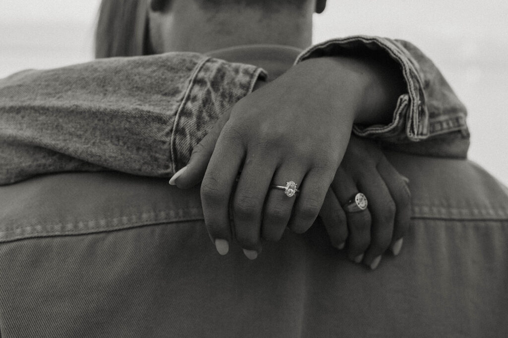 Woman with arms draped over the back of fiancé while wearing engagement ring at Meeks Bay