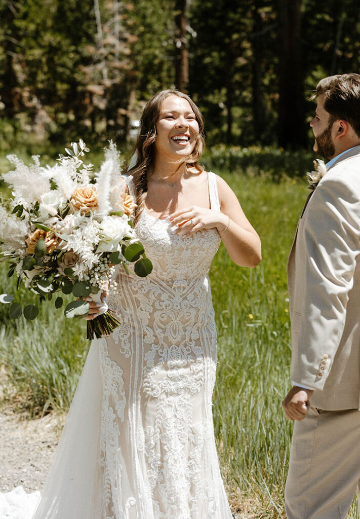 Bride laughing while holding floral bouquet with grass meadow in background in Lake Tahoe