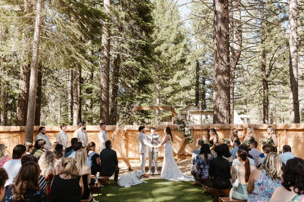 Wedding ceremony in Lake Tahoe with wooden arch and florals while wedding couple holds hands in the center