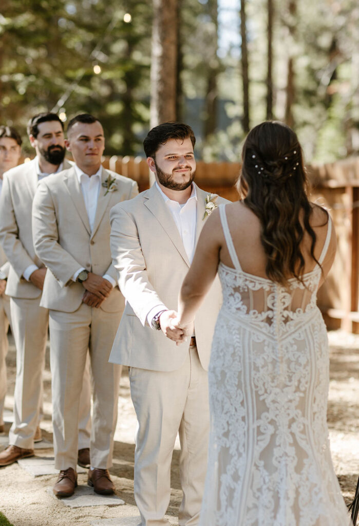 Wedding groom holding hands with bride while smiling during ceremony with groomsmen behind him in Lake Tahoe