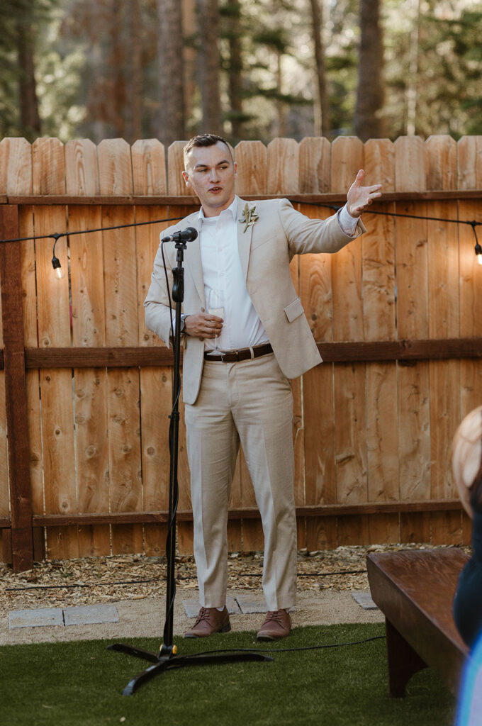 Best man giving speech with wooden fence and lights behind in during wedding reception in Lake Tahoe