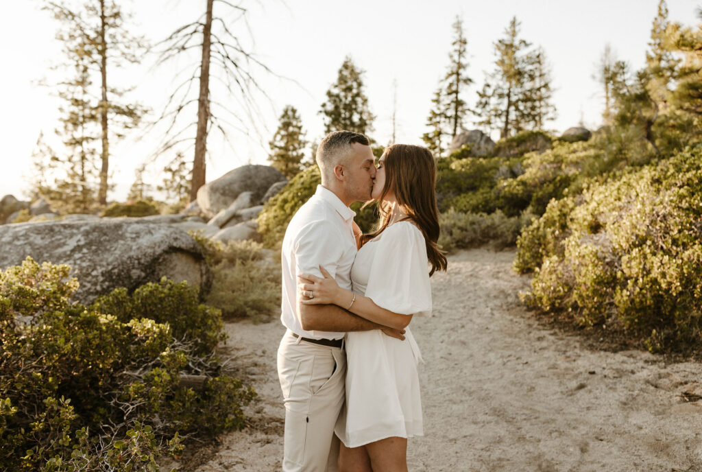 Engagement couple holding each other while kissing on sandy trail surrounded by bushes in Lake Tahoe 