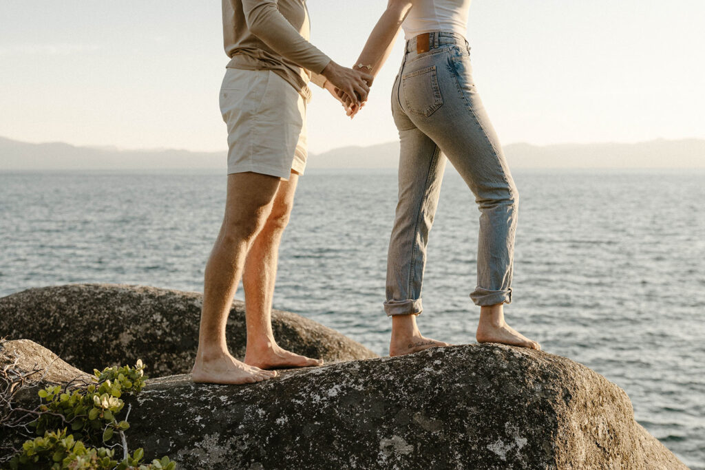 Engagement couples hands and feet as they walk along rocks together next to Lake Tahoe