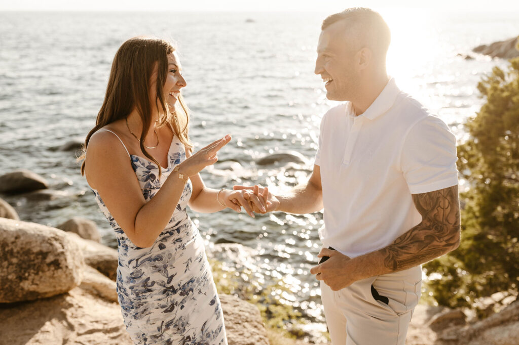 Engagement couple holding hands and smiling at each other after proposal at Lake Tahoe with lake in background