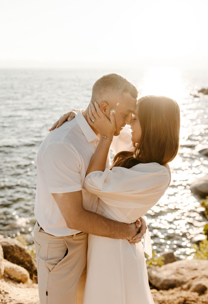Engagement couple holding each other while wearing neutral color clothing with Lake Tahoe in background