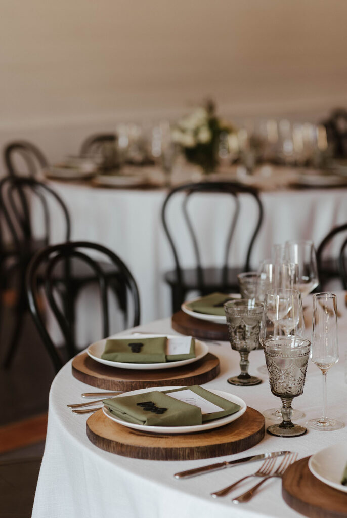 Wedding reception dinner tables with wooden placemats and dull green napkins at French Oak Ranch