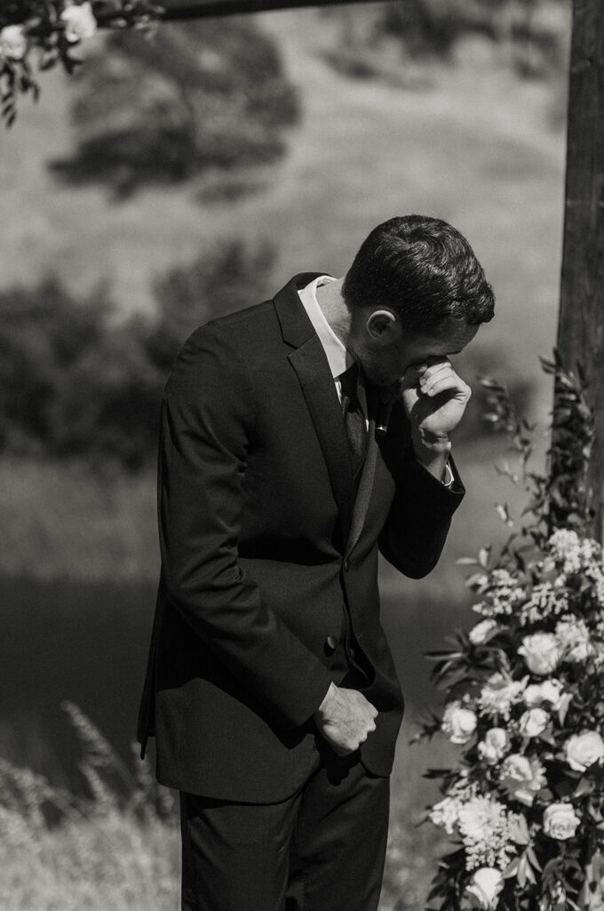Groom emotional and wiping tears while watching bride walk up to wedding ceremony at French Oak Ranch