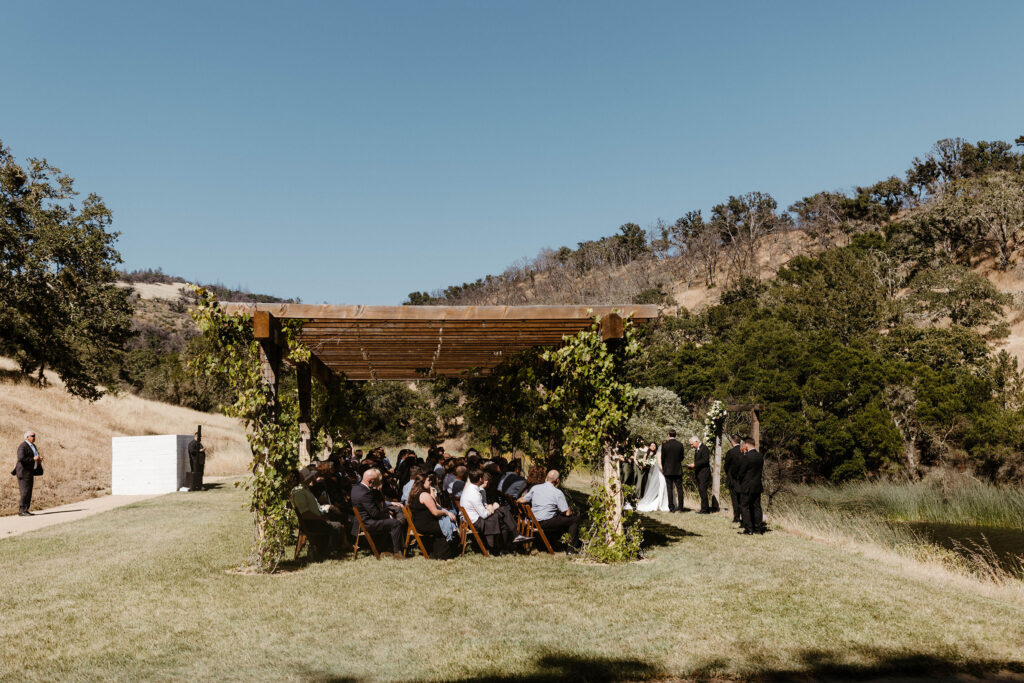 Wedding ceremony at French Oak Ranch underneath wooden gazebo surrounded by hills and trees