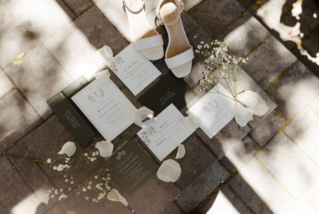 Wedding details and shoes in flat-lay on stone surrounded by white flowers and petals at French Oak Ranch